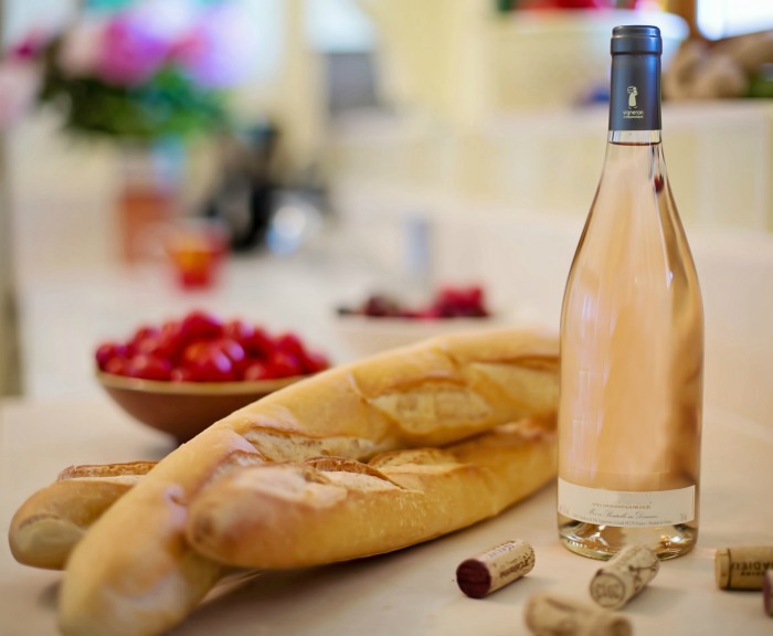 Baguete fatiada, tomates e uma garrafa de vinho.