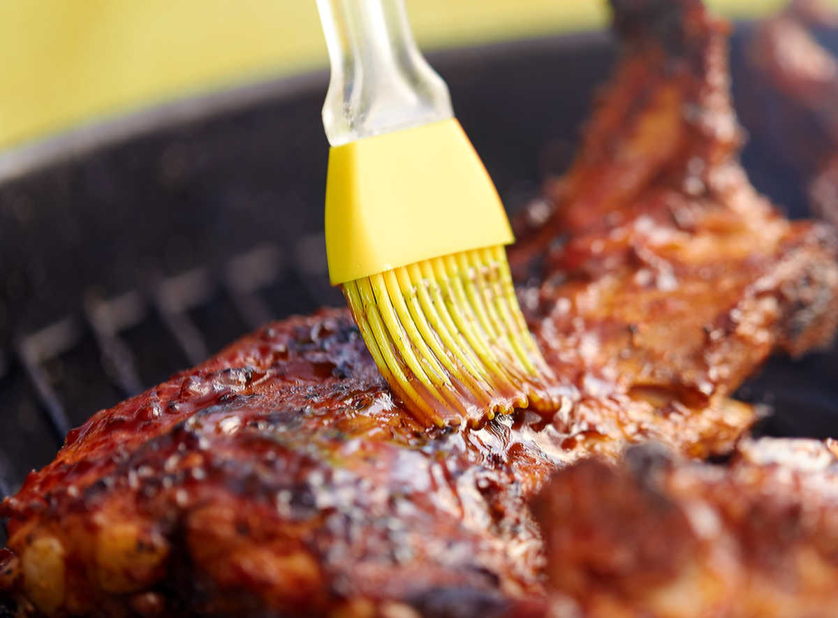 Pincel de silicone amarelo adicionando molho barbecue à carne.