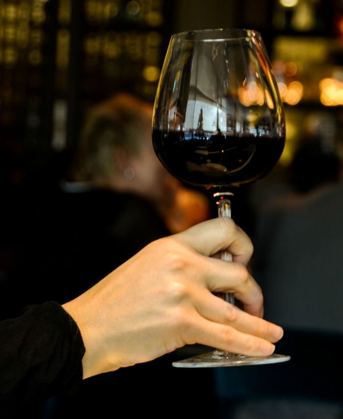 Mão feminina segurando um copo de vinho tinto.