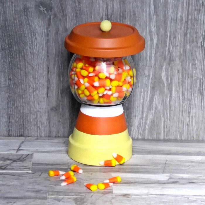 Dispensador de doces de milho feito de um pote de barro e uma tigela de vidro.