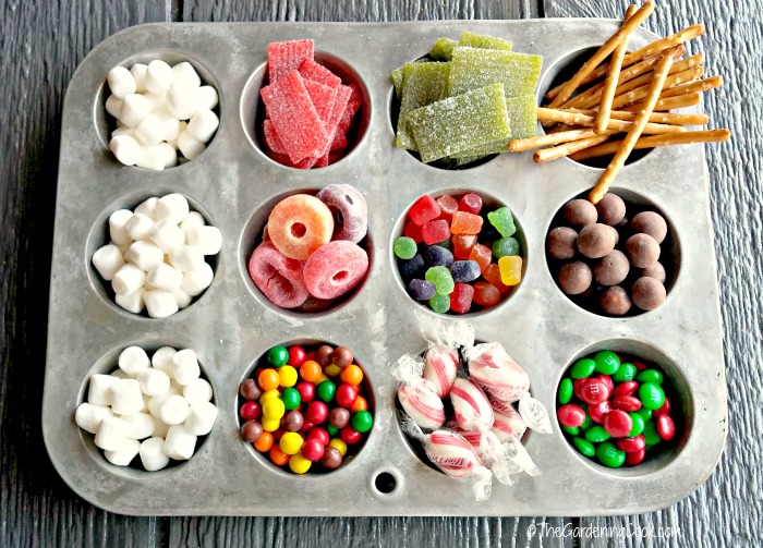 Marshmallows, bala listrada, bolinhas de leite maltado, Skittles, pretzels, gelatinas e M&Ms em uma forma de muffin, prontos para montar uma casa de gengibre.