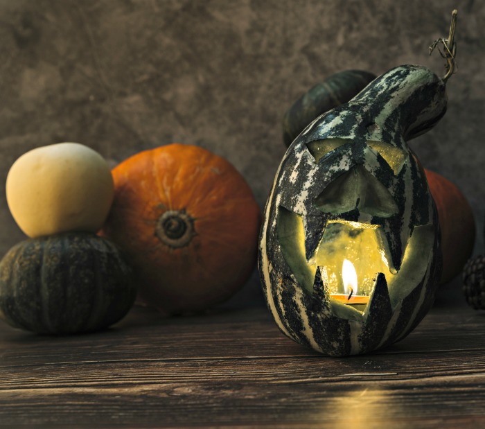 gourd esculpida com uma vela por dentro e abóboras ao lado.