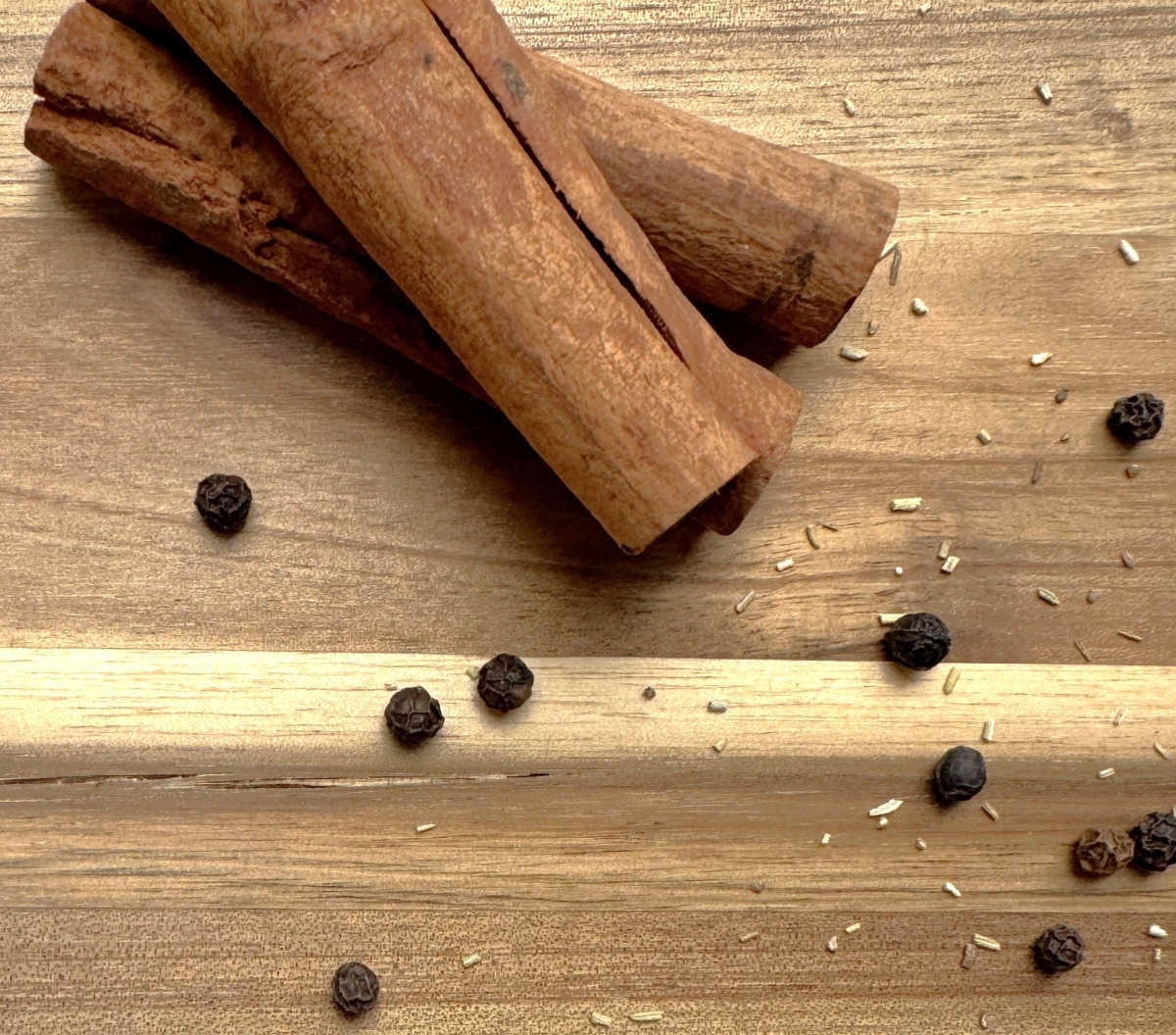 Paus de canela e grãos de pimenta-do-reino sobre uma bancada de madeira.