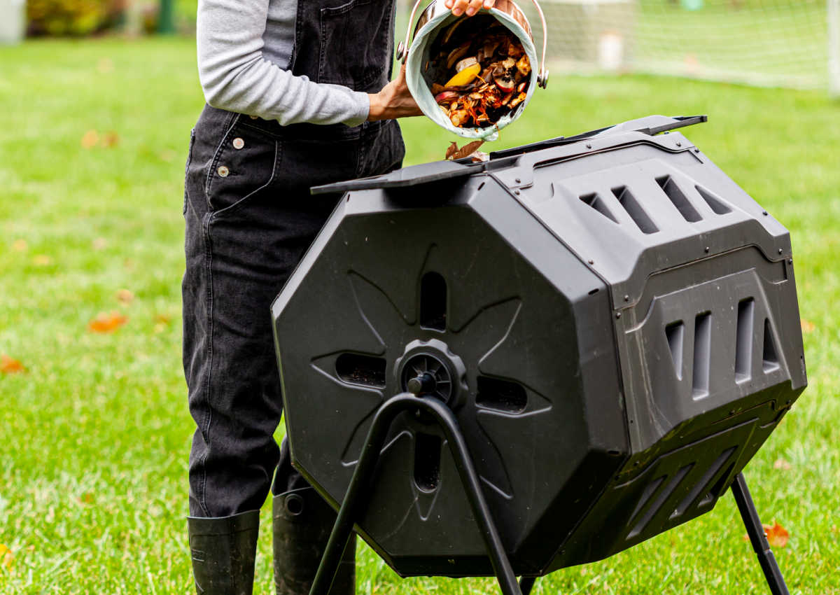 Uma mulher colocando resíduos da cozinha em um compostor giratório para criar um corretivo de solo com composto.