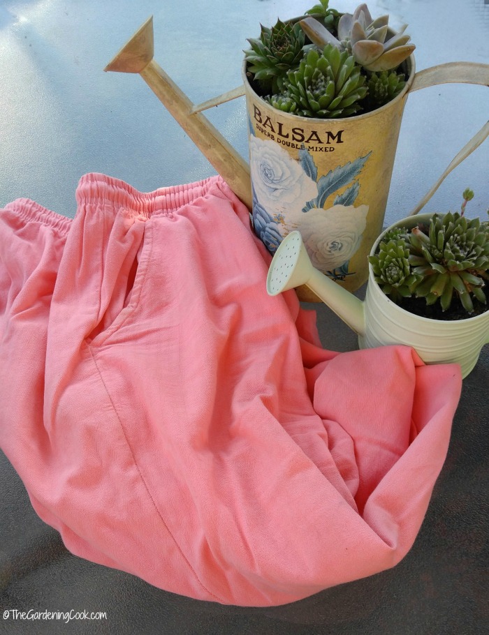 Roupas de algodão em uma cor pêssego perto de alguns regadores com suculentas.