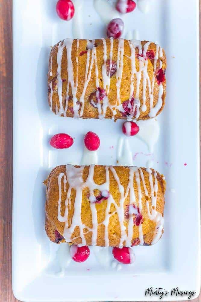Esta receita fácil de Pão Rápido de Abóbora com Cranberry logo se tornará uma das favoritas da família. Coberto com uma cobertura simples, o pão é perfeito o ano todo! Pão rápido de abóbora e cranberry em um prato branco