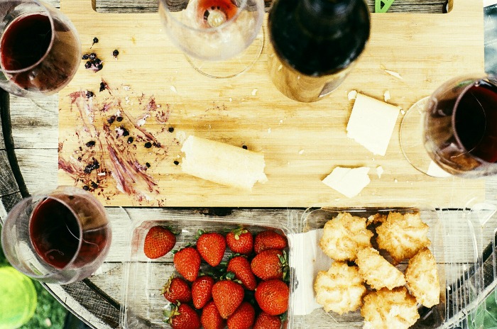 Tábua de corte com taças de vinho e frutas.