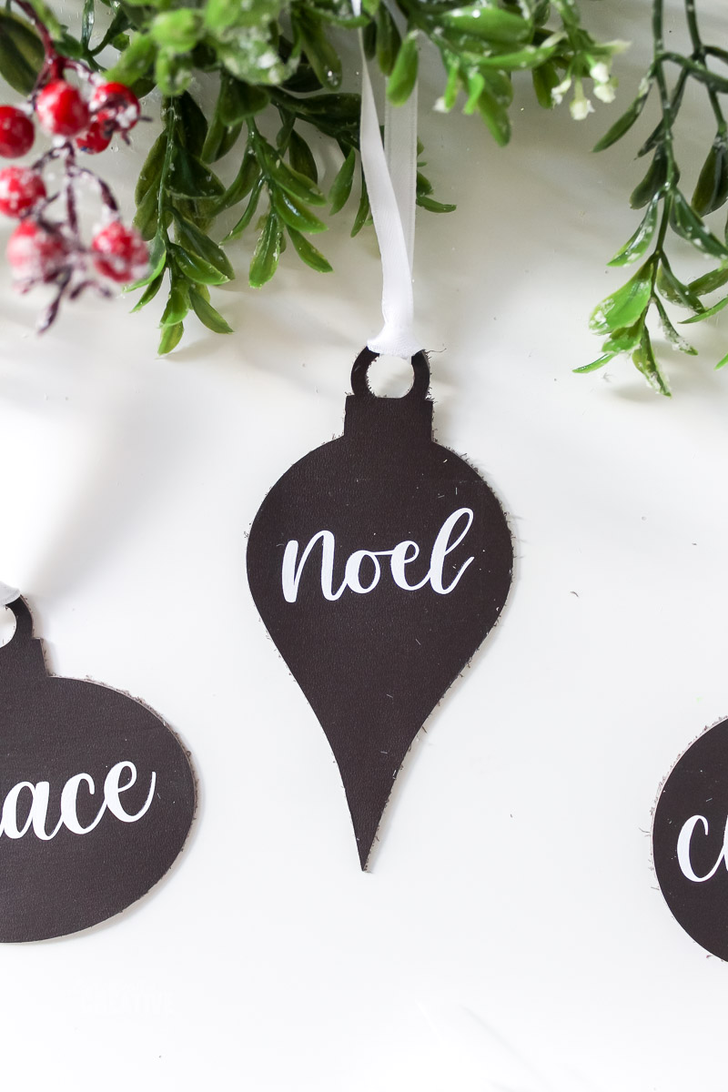 Enfeite de couro Noel sobre mesa branca com folhagens
