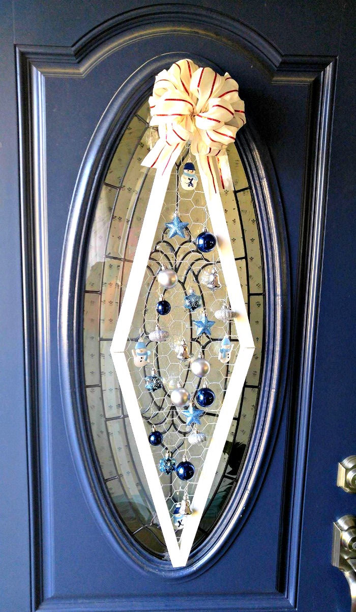 Decoração de porta com ornamento de Natal em uma porta azul com vidro oval.