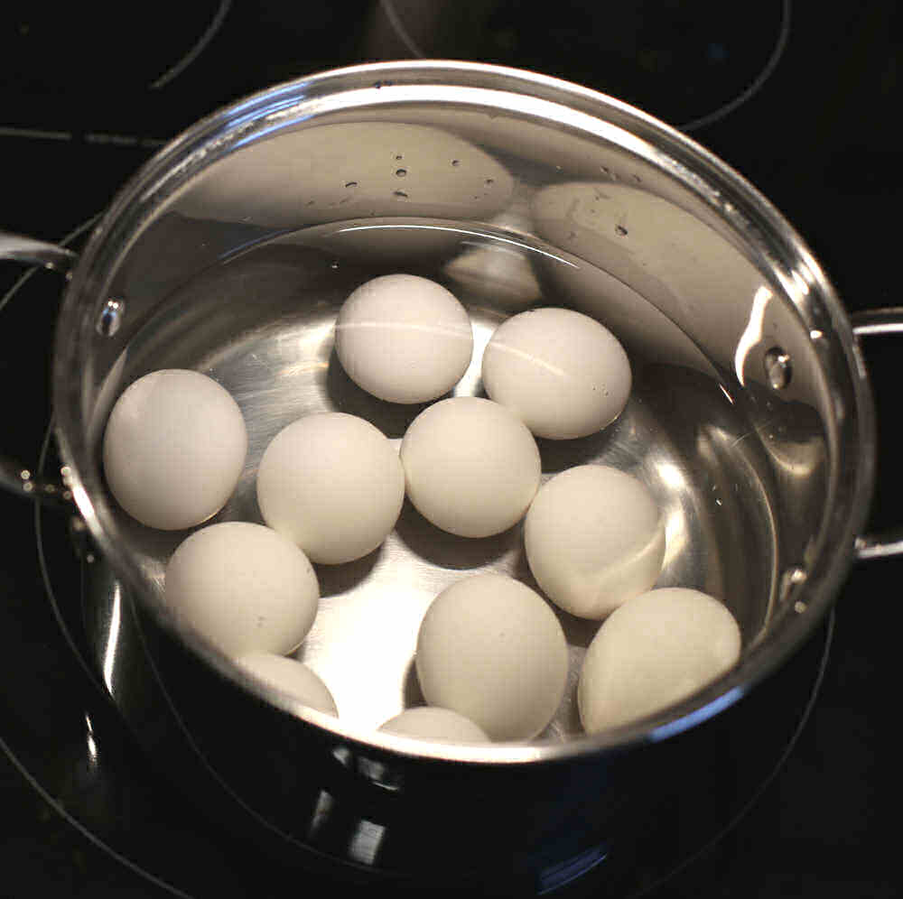 Ovos em uma panela com água fria em um fogão preto.