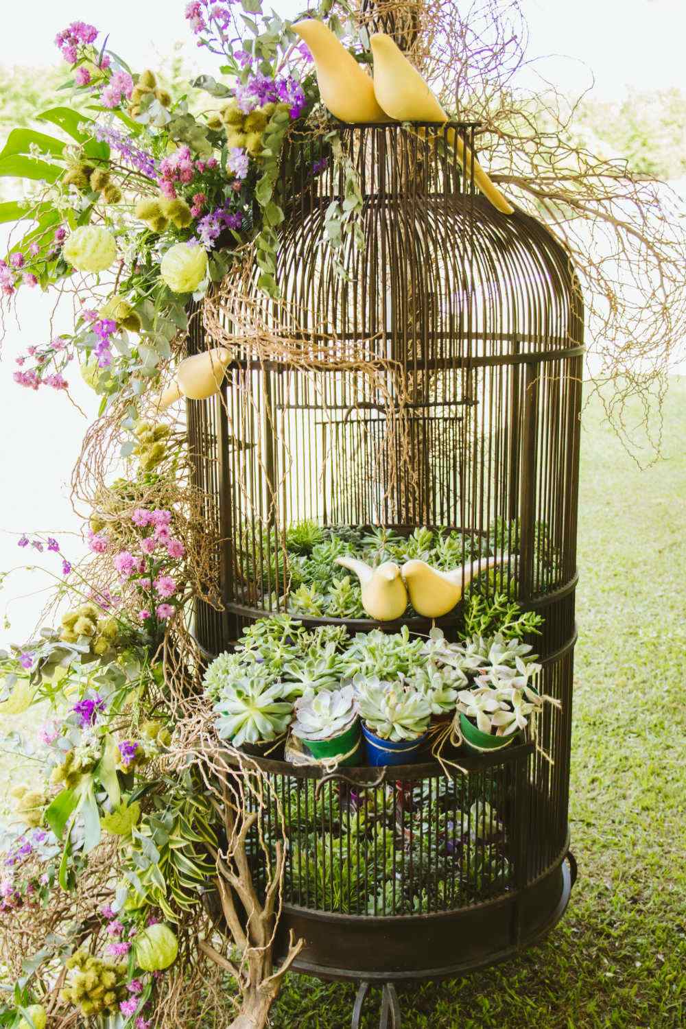 Arranjo elaborado em uma gaiola de pássaro com pássaros, suculentas e folhas e flores de seda.
