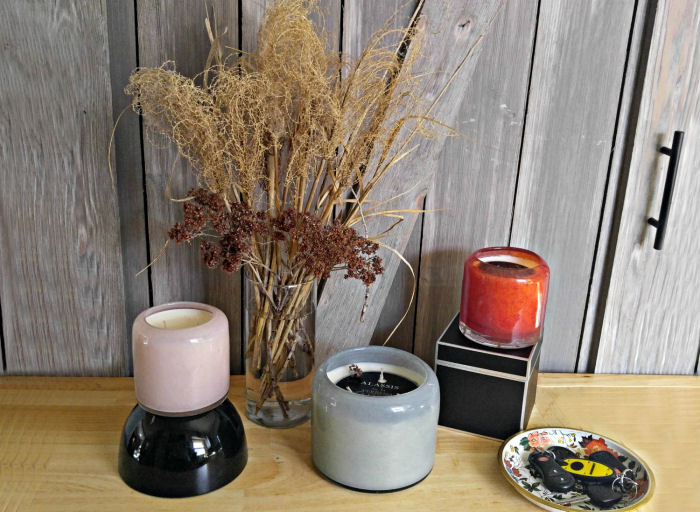 Três velas ao lado de um vaso de flores secas e uma bandeja com chaves para decorar a entrada com velas.