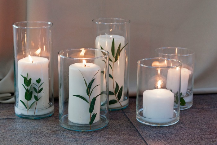 Velas brancas com folhas de eucalipto dentro dos suportes de velas.