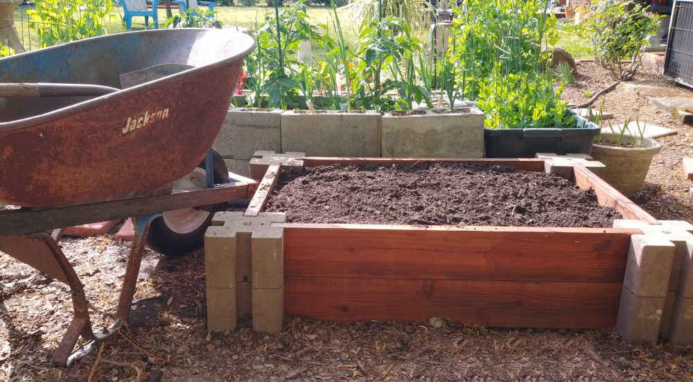 Um carro de mão e uma pá ao lado de uma cama de jardim fácil cheia de solo.