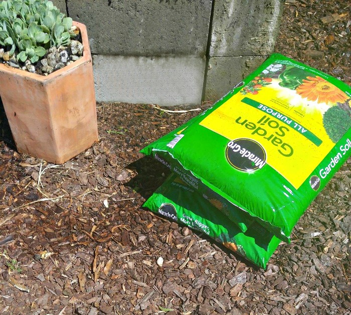 2 bolsas de solo para vasos Miracle Gro ao lado de um canteiro de blocos de concreto.