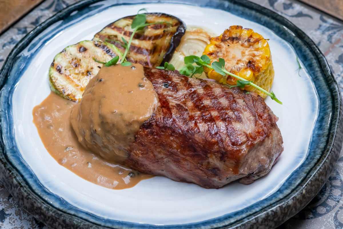 Carne e legumes em um prato com marcas de grelha e molho.