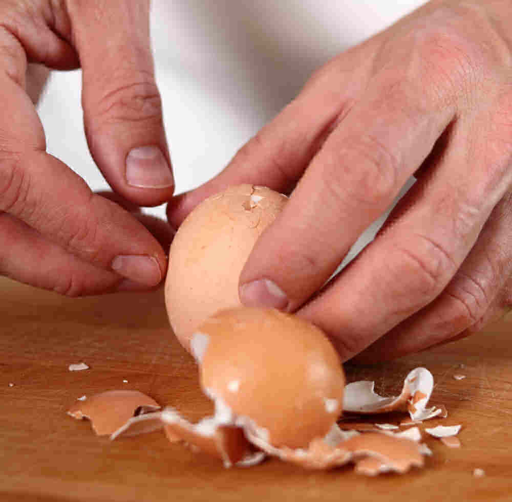 Mãos batendo em um ovo cozido para quebrar a casca.