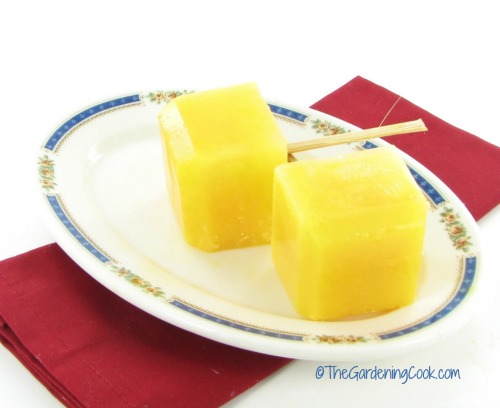 picolés de suco de laranja feitos em formas de gelo de silicone em um prato branco e azul com um guardanapo vermelho.