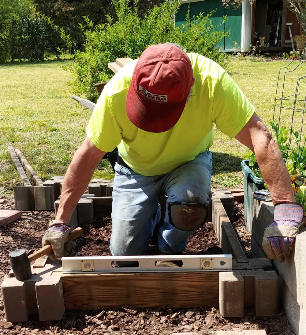 Homem usando um nível de bolha para deixar os lados de uma cama de jardim elevada fácil.