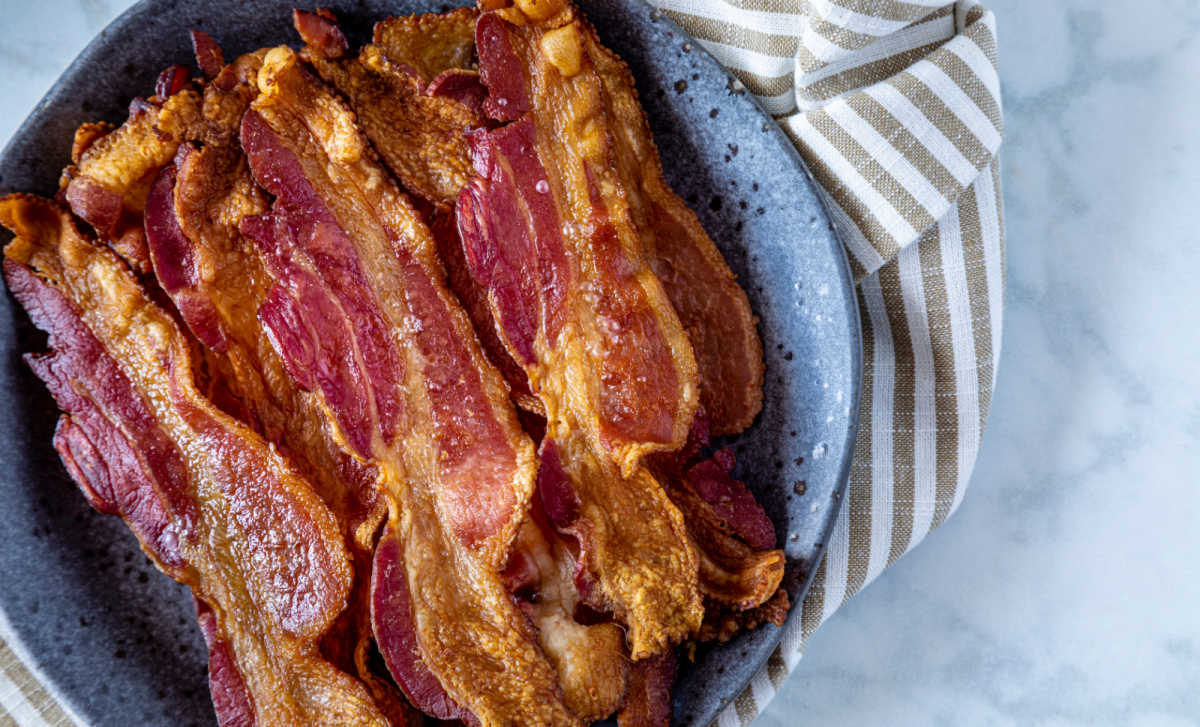 Bacon no forno sem bagunça em uma tigela azul ao lado de uma toalha listrada.