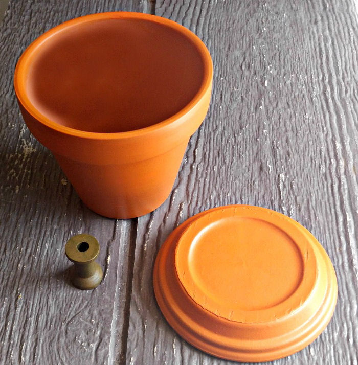 Vaso de barro e prato pintados de laranja e um carrete de madeira pintado de verde amarelado.
