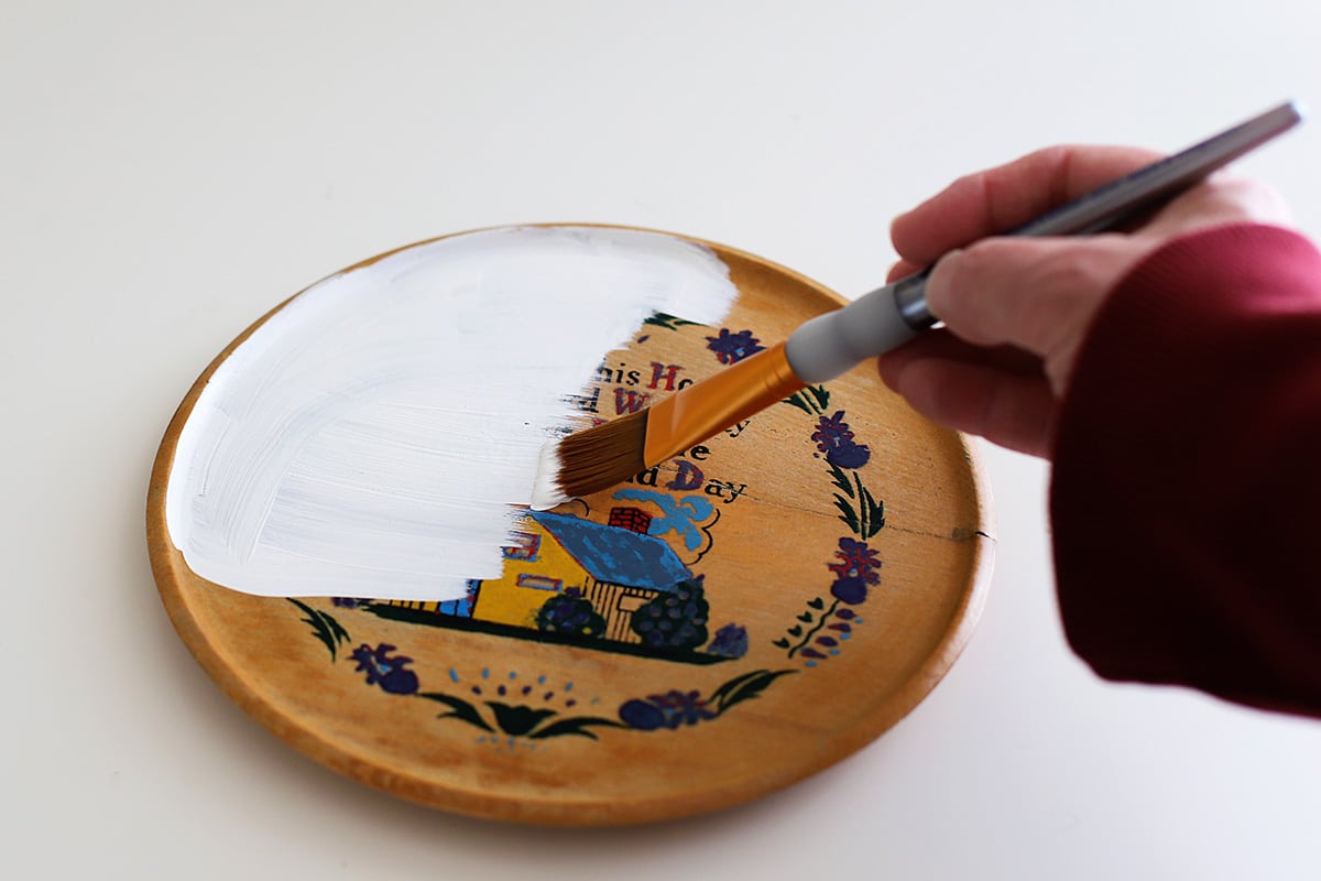 Pintando uma placa de madeira com tinta branca.