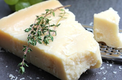 Um bloco de queijo parmesão coberto com tomilho ao lado de um ralador de queijo.