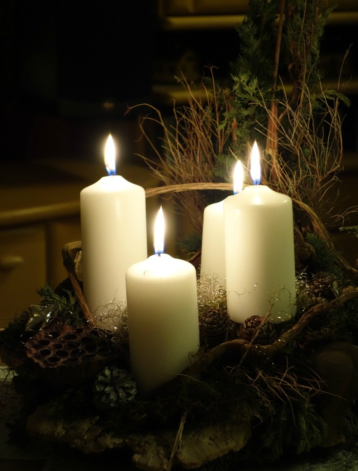 Velas brancas acesas em uma cesta com folhagens secas.