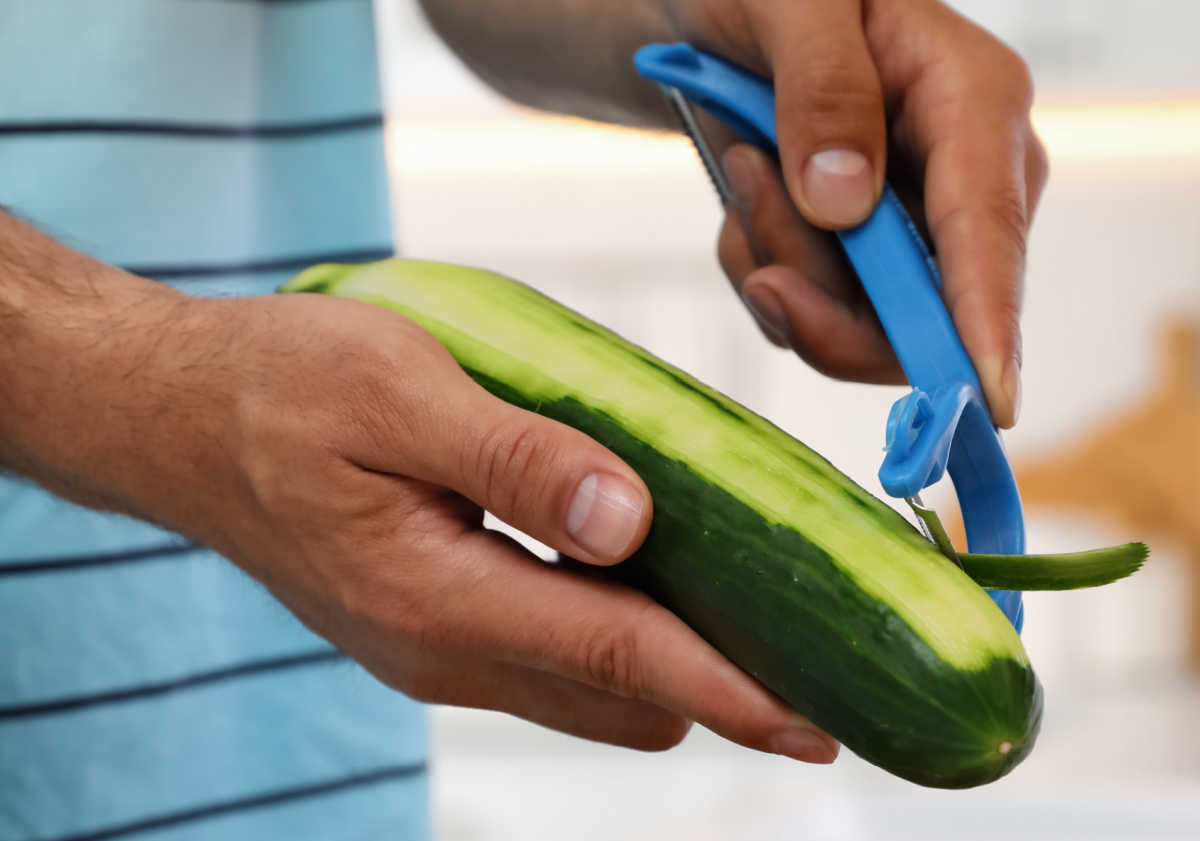 Homem em uma camisa azul descascando um pepino.