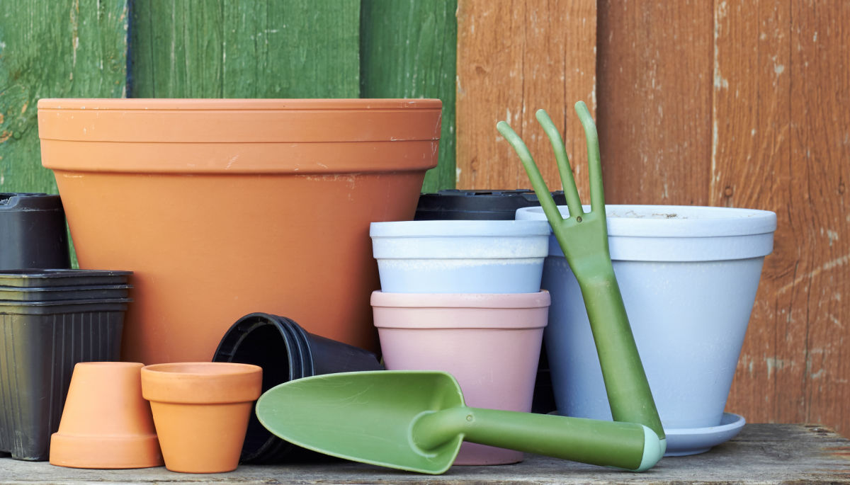 Um grupo de vasos de barro e vasos plásticos limpos com ferramentas de jardinagem, guardados em um galpão.
