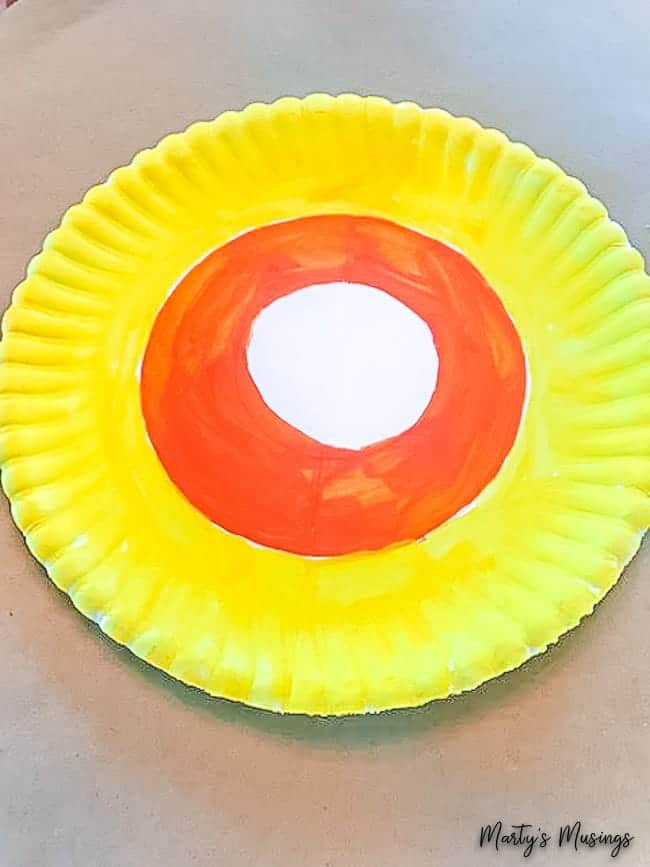 Quer um artesanato fácil de Halloween ou de outono? Este banner de candy corn é super fácil e feito com um prato de papel! Perfeito para crianças! prato de papel pintado com círculos laranja e amarelo