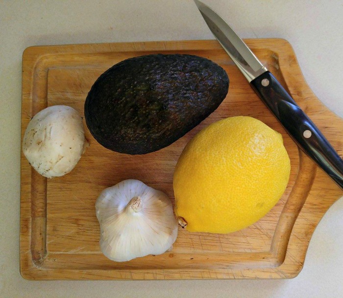 Abacate, limão, alho e cogumelo em uma tábua de cortar com uma faca.