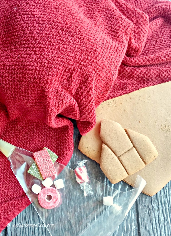 Pedaços de gengibre, doces, saco de confeitar e um pano de prato limpo cobrindo a tigela de glacê real.
