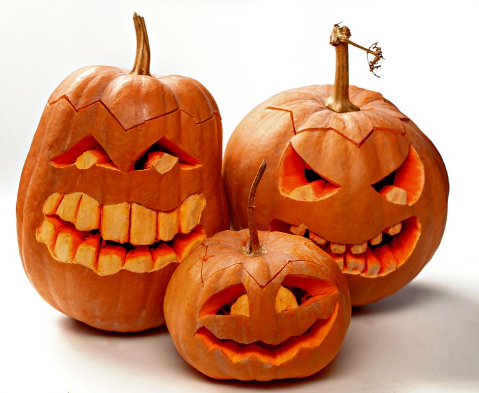 Trio de abóboras sorridentes esculpidas com dentes grandes.