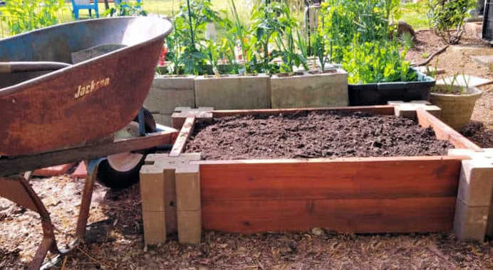 Um carrinho de mão e uma pá com composto ao lado de um canteiro elevado no início da primavera.