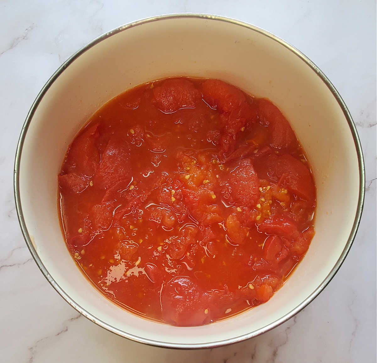 Tomates torrados triturados para molho em uma tigela branca em uma bancada de mármore.