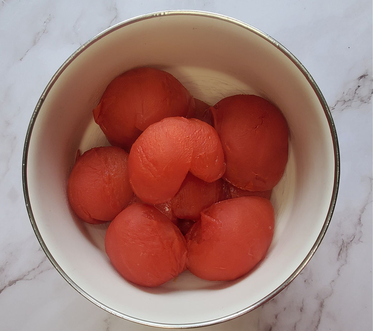 Metades de tomates beefsteak assados em uma tigela de cerâmica branca em uma bancada de mármore.