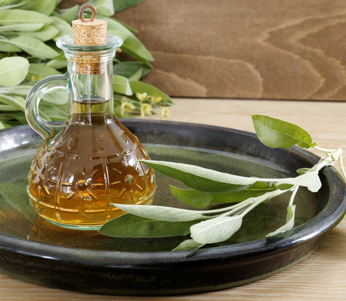 Infunda sálvia com vinagre. Vinagre de sálvia em uma garrafa de vidro com sálvia fresca em uma bandeja de servir.