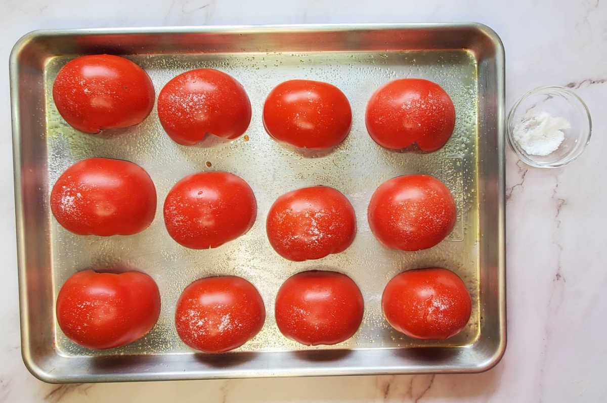 Tomates beefsteak cortados ao meio, temperados com sal em uma grande assadeira.