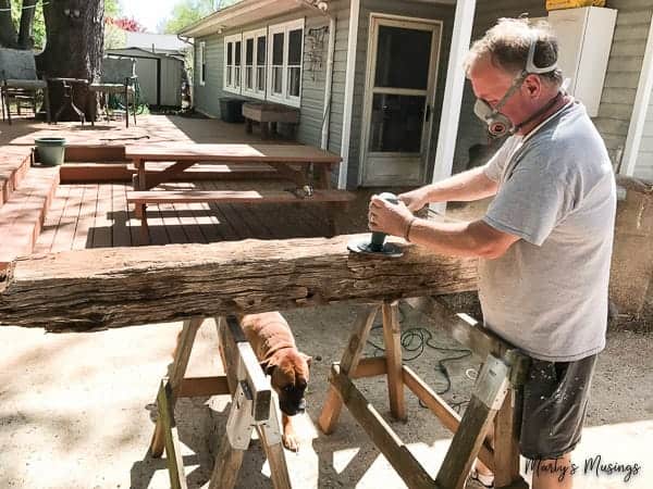 Homem com máscara lixando tora de madeira de celeiro