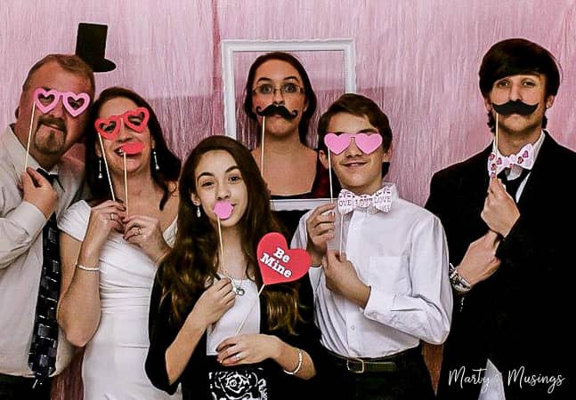 Estas decorações de 25º aniversário são perfeitas para uma cerimônia de renovação de votos fácil e econômica, celebrando 25 anos de casamento juntos! Cantinho de fotos do Dia dos Namorados com a família celebrando bodas de prata