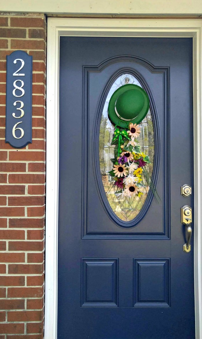 Guirlanda de porta do Dia de São Patrício em uma porta azul de uma casa de tijolos com os números 2836.