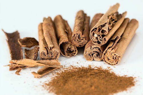 Canela em pau ao lado de um pouco de canela em pó.