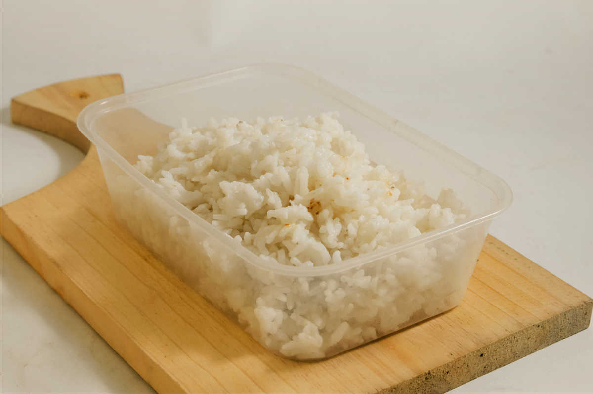 Recipiente de arroz cozido sobrado em uma tábua de corte.
