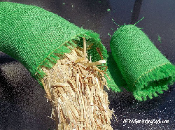 Uma guirlanda de palha coberta com juta verde ao lado de um rolo de tecido de juta verde.