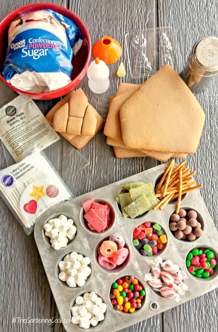 Doces em formas de muffin, peças de casa de gengibre, uma peneira para açúcar de confeiteiro e outros materiais para fazer sua própria casa de gengibre.