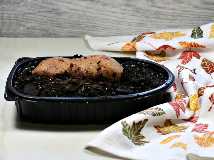 Uma batata-doce orgânica no solo, em uma bandeja plástica preta, ao lado de uma toalha estampada.