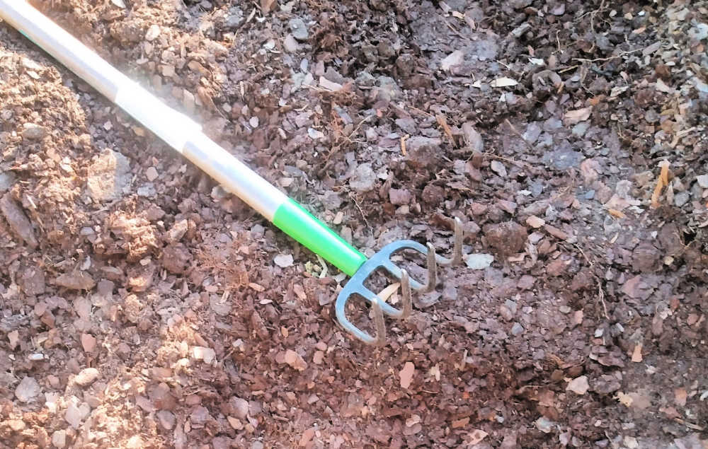 Um arado de cabo longo afrouxando o solo para construir camas de jardim elevadas.