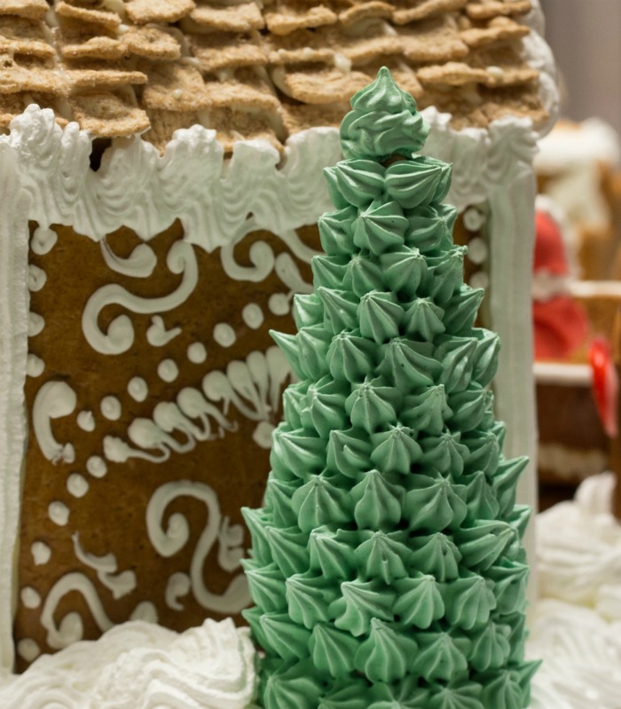 Uma árvore de Natal feita de cone de sorvete coberta com estrelas de cobertura verde perto de uma casa de gengibre decorada.