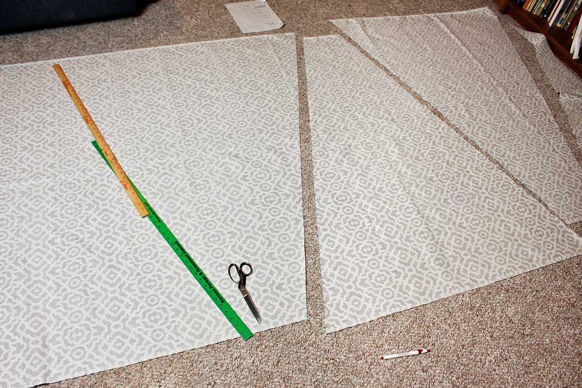 Painéis triangulares para um Toldo Teepee DIY para Crianças sendo cortados de um tecido com uma tesoura de tecido, medidos com uma fita métrica.